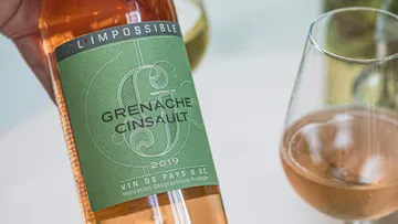 Flasche Wein hält, etikettiert mit Grenache Cinsault.