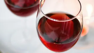 Red wine glasses are set against a blurred, cozy environment.