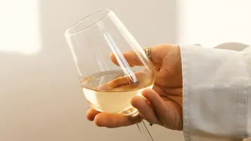 Ein Glas mit weißem Wein wird gehalten.