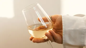 Ein Hand hält ein Weinglas mit hellem Getränk.