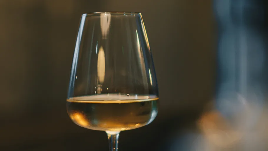 Wine glass stands with golden drink in the background.