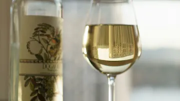 White wine in glass next to a decorated bottle.