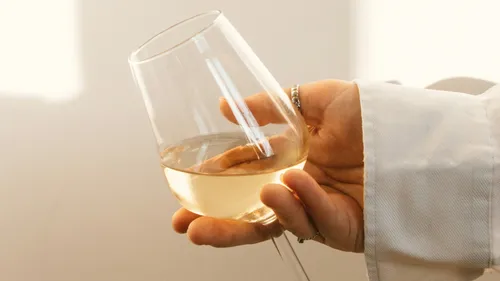 A glass of white wine is held in one hand.