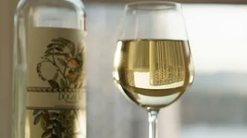 White wine in a glass is next to a bottle.