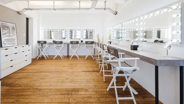 Helle Make-up-Station mit Stühlen und großen Spiegeln.