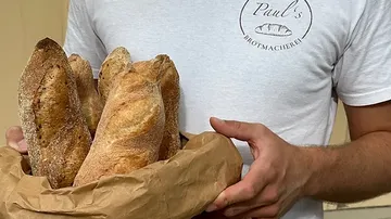 A man is holding a bread basket with freshly baked bread.