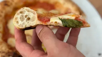 One hand holds a slice of pizza with fresh basil.