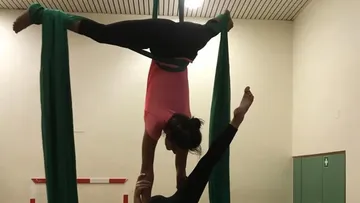Two acrobats are working on green cloths in a room.