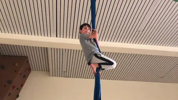 Ein Junge klettert an einem blauen Tuch hoch, drinnen.