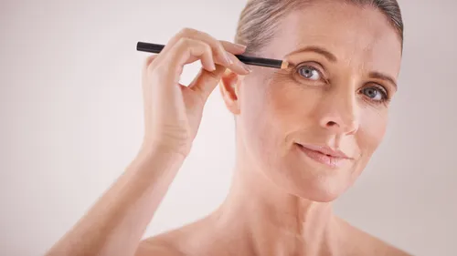 Woman applying makeup with a pen against a white background.