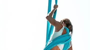 Woman swinging on a blue cloth against a bright sky.