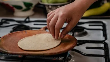 One hand places a tortilla on a hot pan.