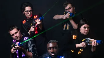 Five people aim toy guns in the dark.