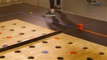 Wooden game floor with holes; player kicks a ball.