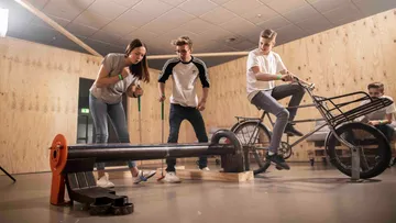 Three people interact with a mechanical device in the room.