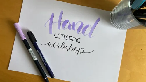Hand lettering workshop on paper surrounded by pens.