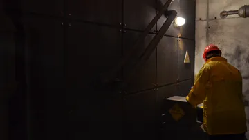 Worker wearing yellow protective clothing examines a machine in the dark.