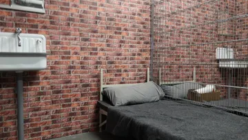 A bed is in a cage room with brick walls.