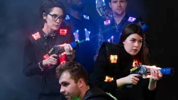 People play laser tag in a dark environment with neon lights.