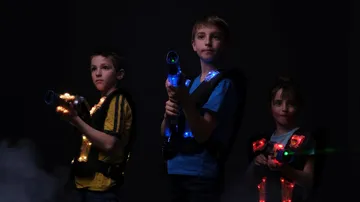 Three children hold glowing weapons in a dark room.