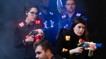 Menschen mit leuchtenden Spielzeugwaffen in einer dunklen Umgebung.