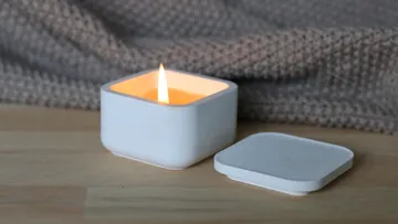 Weiße Kerze brennt auf Tisch, daneben der Deckel.