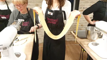 A woman keeps fresh, long dough in a kitchen.
