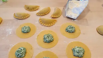 Teigkreise mit Spinatfüllung werden auf Holzbrett vorbereitet.
