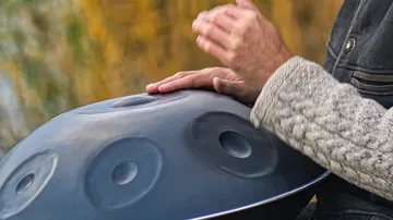 Hände spielen auf einem Hang Drum in natürlicher Umgebung.