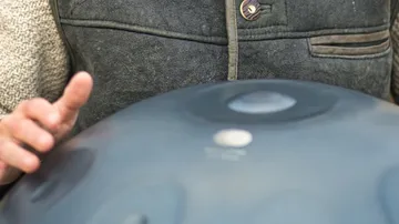A man plays a handpan with one hand.
