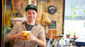 Ein Mann lächelt und hält ein Bierglas in einer Bar.