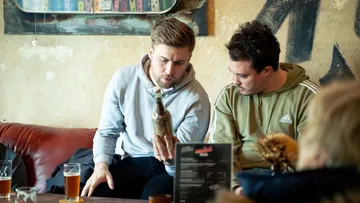 Two men look at a bottle in a café.