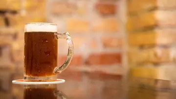 A beer mug stands on a trivet surrounded by stonework.