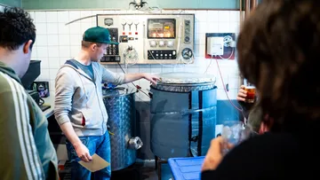 A man points to a large container in a brewery.