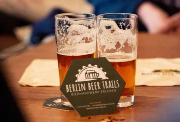 There are two glasses of beer on a table with a flyer.