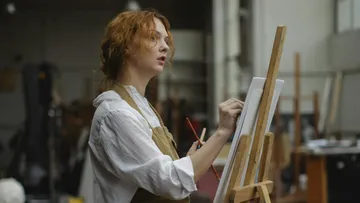 Künstlerin malt an einer Leinwand in einem Atelier.