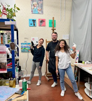 Three people are laughing in an art studio.
