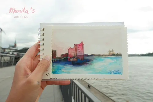 Eine Hand hält ein Aquarell eines Hafens am Wasser.