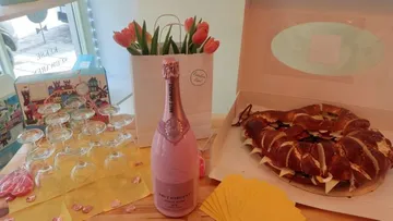 Champagne bottle and pretzel are lying on a table with flowers.