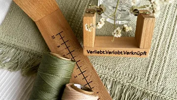 Holzlineal, Garnrollen und Vase auf einem texturierten Untergrund.
