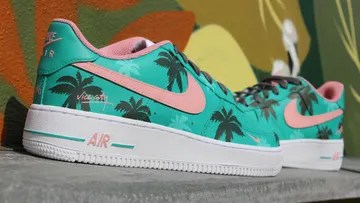 Turquoise sneakers with palm motifs stand in front of a colorful wall.