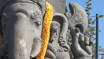 Stone Ganesha statue with yellow flower wreath outdoors.
