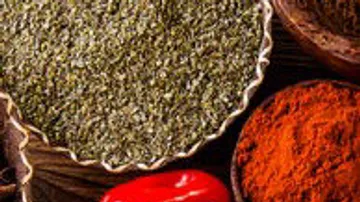 Spices in bowls, including red peppers, on a wooden background.