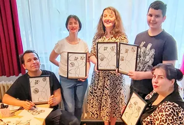 Five people hold drawings in a bright room.