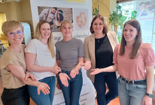 Five women show rings in front of an advertising banner.