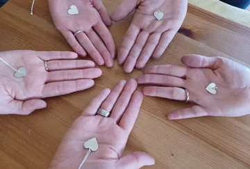 Fünf Hände zeigen silberne Herzanhänger auf Holzoberfläche.
