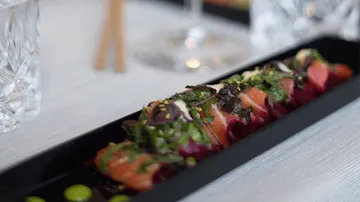 Sushi-Rolle liegt auf schwarzem Teller, umgeben von Dekoration.
