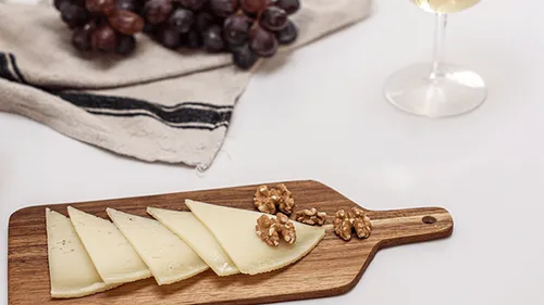 Käse auf einem Brett, umgeben von Trauben und Walnüssen.