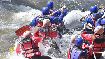 Personen paddeln in einem Boot durch raue Gewässer.