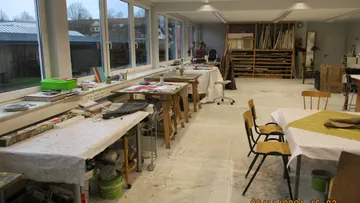 Künstlerisches Studio mit Tischen, Stühlen und Malmaterialien.